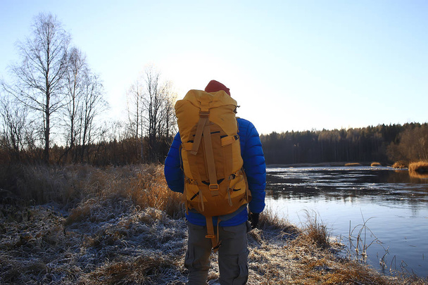 traveler with a backpack by the river / tourist guy on a northern hike, winter trip - Photo, image