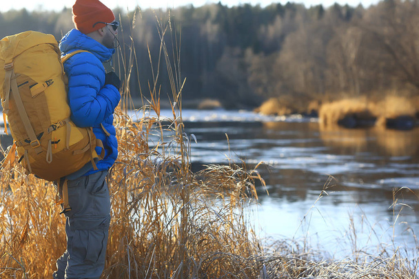 traveler with a backpack by the river / tourist guy on a northern hike, winter trip - Photo, Image