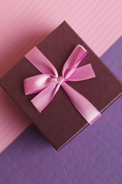 Pequeña caja de regalo con cinta rosa y lazo sobre fondo rosa y púrpura, foto vertical, vista superior
 - Foto, imagen