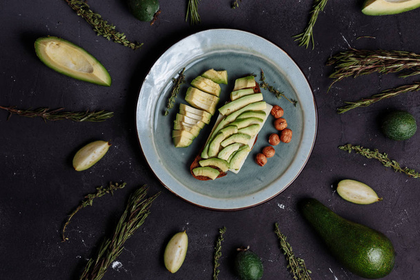 Close-up of avocado slices on rye bread and hazelnuts in a plate on a black background - Fotó, kép