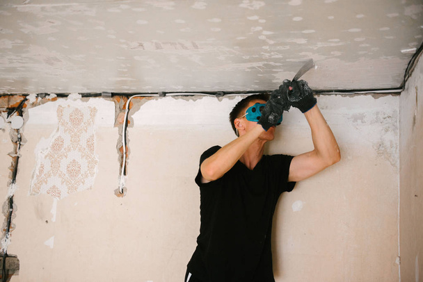 A man removes old paint from the ceiling with a spatula - Foto, imagen
