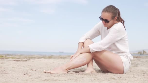 Een vrouw zit bij de zee. ze smeert haar benen met zonnebrand Cream - Video