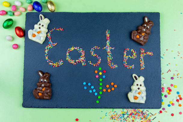 Easter concept multicolored candies are laid out in the form of Easter on a dark blue background with chocolate bunny and eggs - Photo, Image