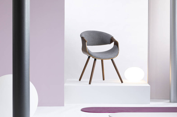 Real photo of a simple, white and purple room interior with a gray chair on a podium - Photo, Image