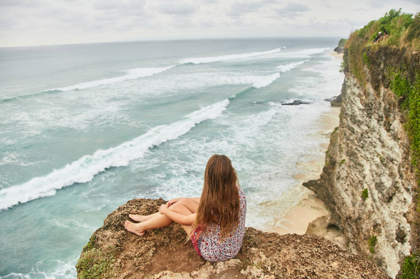 Una joven está sentada en un acantilado. Bali, Uluwatu
.  - Foto, Imagen