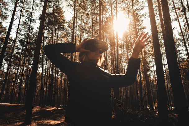 Woman in forest with virtual reality headset looking straight and trying to touch something with her hand - Photo, Image