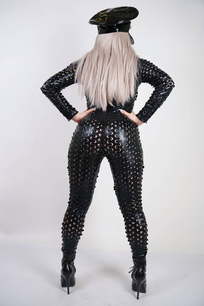 cruel fashionable bdsm lady with curves dressed in black catsuit with sexy holes and posing on a white background in the Studio - Photo, image