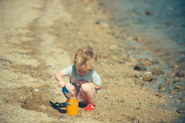 Lapset leikkivät rannalla tekstillä. Söpö pikkupoika leikkii hiekalla rannalla. Loma. Merellä vietetty aika
. - Valokuva, kuva