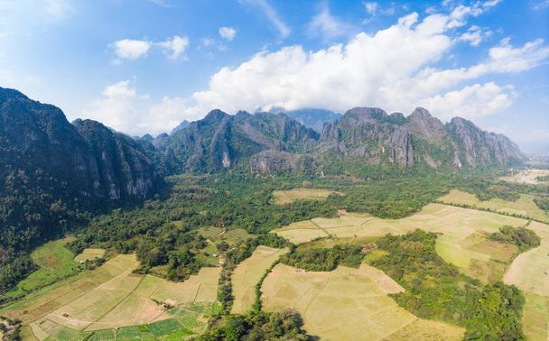 Aérea: destino de viaje de mochilero Vang Vieng en Laos, Asia. Cielo dramático sobre acantilados escénicos y pináculos rocosos, valle de arrozales, paisaje impresionante
. - Foto, imagen