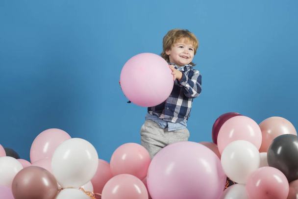 Cute smile from little boy holding big, pink ballon on blue background. Little child is going to throw somebody his ballon. Color background contrast between blue background and pink ballons - Photo, Image