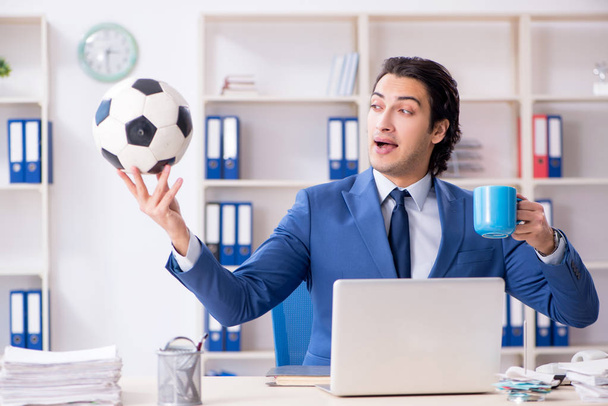 Mladý pohledný podnikatel s fotbalovým míčem v kanceláři  - Fotografie, Obrázek