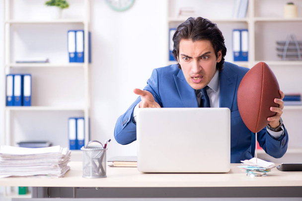 Fiatal, jóképű üzletember rögbi labdát az irodában - Fotó, kép