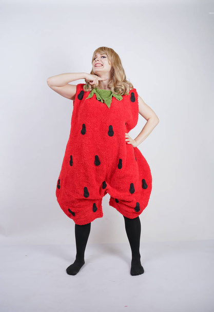 caucasian emotive blonde girl in a huge plush suit of red strawberry on a white background in the Studio - Valokuva, kuva