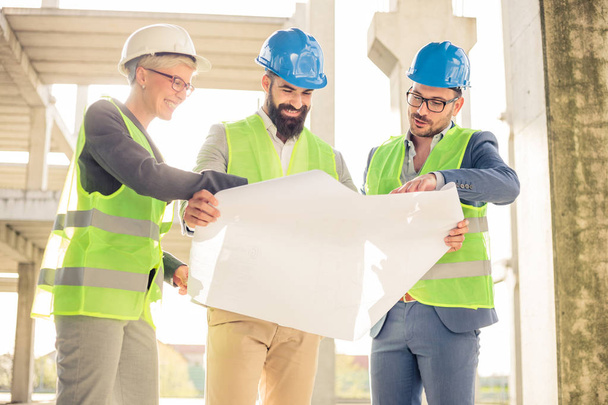 Mixed group of engineers or business partners at construction site, working together on building's blueprint. Architecture and teamwork concept. - Фото, изображение