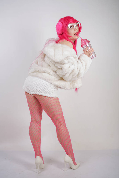 sexy chubby pink haired woman wearing sexy lingerie and fur jacket with plastic sunglasses on white studio background alone - Foto, Imagem