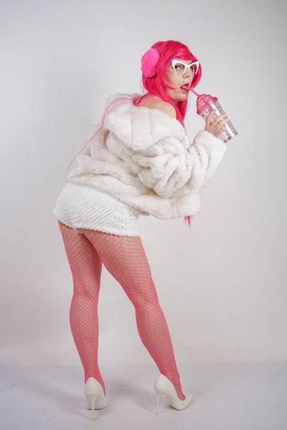 sexy chubby pink haired woman wearing sexy lingerie and fur jacket with plastic sunglasses on white studio background alone - Foto, immagini