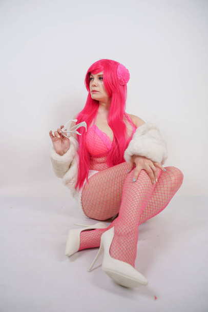 sexy chubby pink haired woman wearing sexy lingerie and fur jacket with plastic sunglasses on white studio background alone - Fotó, kép