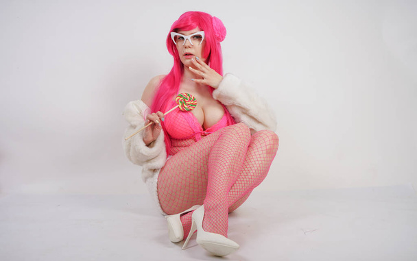 sexy pummelige pinkhaarige Frau trägt sexy Dessous und Pelzjacke mit Plastiksonnenbrille auf weißem Studiohintergrund allein - Foto, Bild