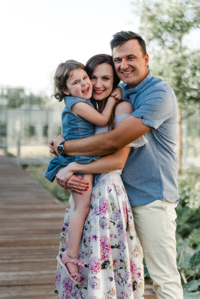 Happy young family with little daughter. Smiling young parents and their child. Cute little girl and her beautiful parents. Family with little daughter resting and having fun - Фото, изображение