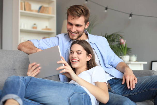 Young couple watching media content online in a tablet sitting on a sofa in the living room. - Valokuva, kuva