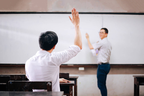 Young adult male student raising hands up in the air to ask questions from another male teacher. - Foto, imagen