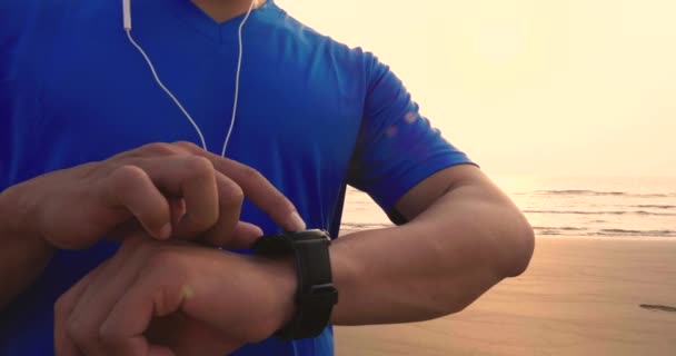 jonge man draait op het strand en het controleren van hartslagmeter op horloge - Video