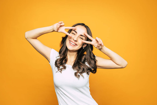 Happy as Larry! An orange background with a beautiful girl with curly brown hair, brilliant smile in white casual T-shirt in front of it. - Zdjęcie, obraz