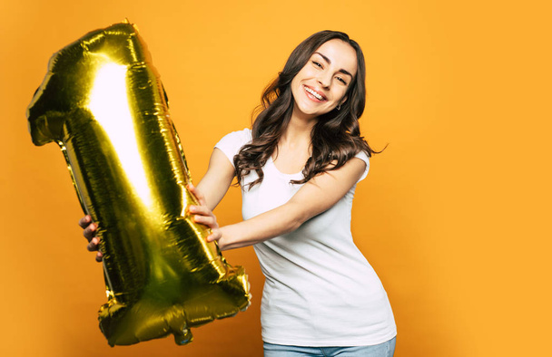 Got it! A girl on the photo is celebrating her personal achievement with gold balloon in a shape of number one. - Foto, imagen