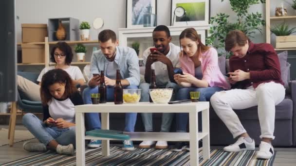 Grupo multirracial de amigos usando teléfonos inteligentes que tocan la pantalla en el sofá en casa
 - Metraje, vídeo