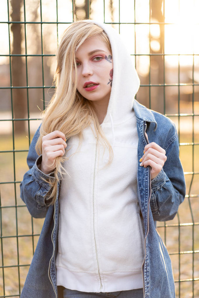 Young Woman with temporary painted flowers on the face. teenage girl with long blond hair wear jeans jacket and hoody - Foto, Imagen