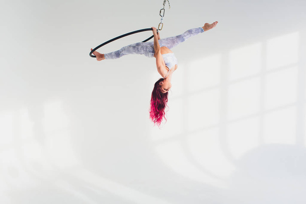 молода руда жінка виконує акробатичні елементи в повітряному кільці на білому тлі
. - Фото, зображення