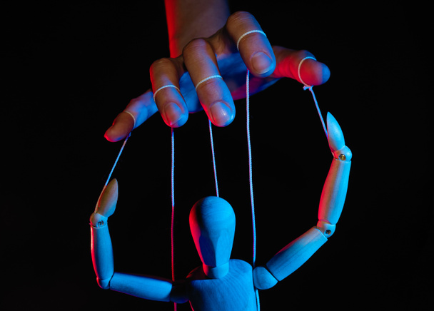 Поняття контролю. Маріонетка в людській руці. Об'єкти кольорові на червоне і синє світло. - Фото, зображення