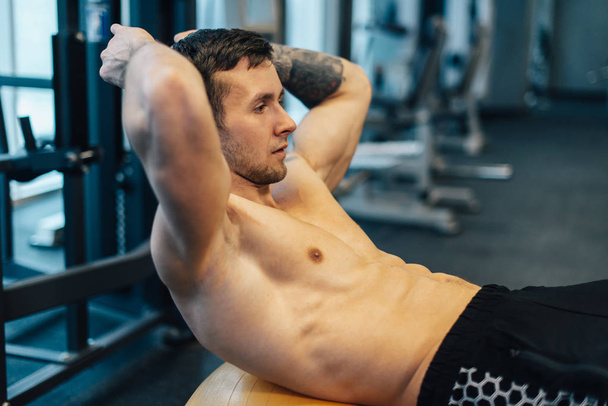Young muscular man trains ab muscles using gym ball, close up - Fotografie, Obrázek
