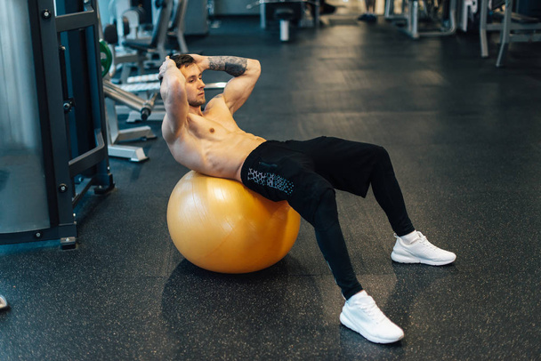 Young muscular man trains ab muscles using gym ball - Foto, afbeelding