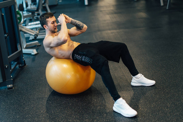 Young muscular man trains abdominal muscles using exercise ball - Foto, afbeelding