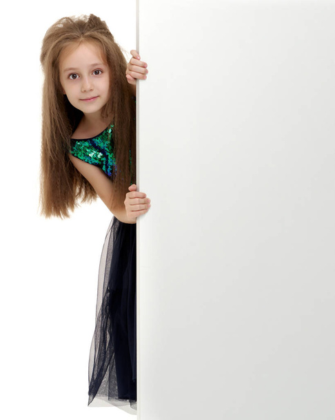 A little girl is looking from behind an empty banner. - Foto, Imagen