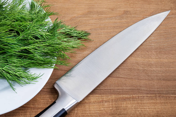Sharp professional chef knife on a bunch of fresh green dill - Foto, afbeelding