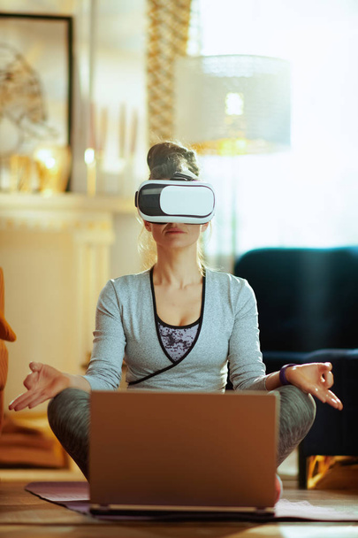 relaxed young woman in sport clothes with laptop in VR gear at modern home. - Foto, imagen