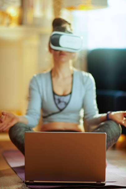 Closeup on laptop and fit woman doing yoga with laptop in VR gear at modern home. - Foto, Imagen