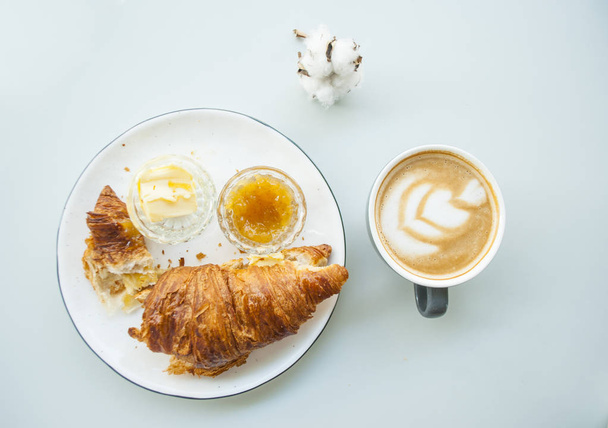 Falt lay of fresh croissant with jam, butter and cappuccino with beautiful latte art on grey table in a cafe. Morning routine. - Фото, зображення