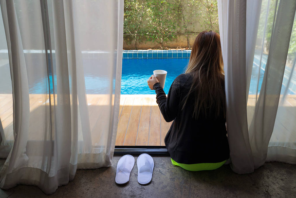 Mujer asiática sentada en piscina privada sosteniendo taza blanca
 - Foto, Imagen