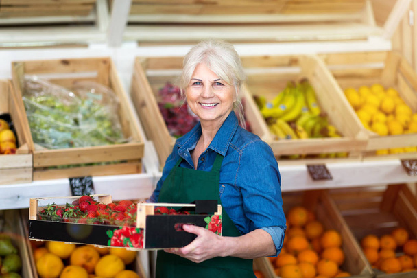 Shop assistant holding box with fresh strawberries in organic produce shop - Photo, Image