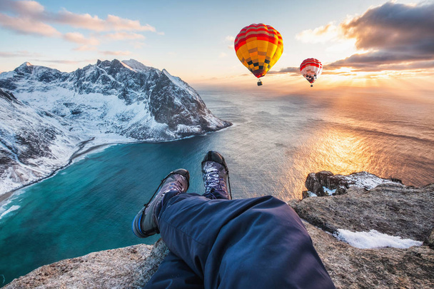 Человек перекрещивает ноги сидя на скале хребта с воздушным шаром
  - Фото, изображение