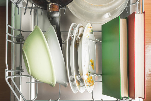 汚れた皿と緑と赤の本は台所の食器洗い機にあります - 写真・画像