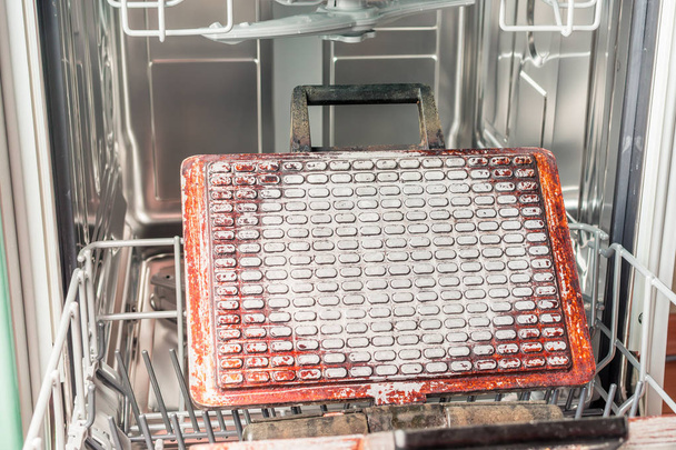 Грязная вафельница лежит на полке посудомоечной машины.
 - Фото, изображение