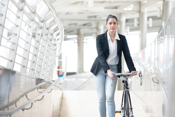 Joven mujer de negocios con bicicleta caminando por la acera al aire libre i
 - Foto, Imagen