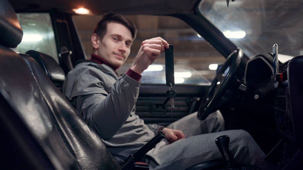 Φωτογραφία από την πλευρά του αρσενικού οδηγού κρατώντας τα κλειδιά που κάθονται στο αυτοκίνητο. - Φωτογραφία, εικόνα