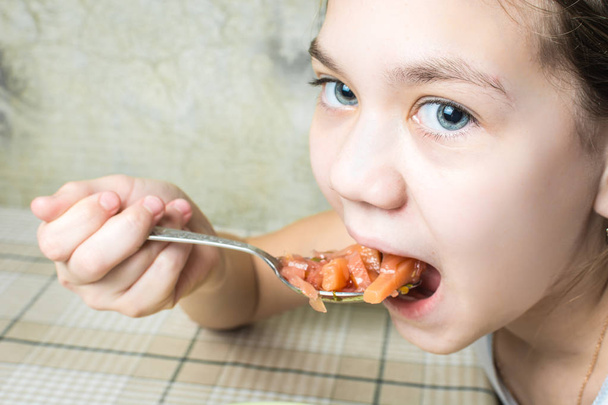 Beautiful girl eats red soup soup from the plate at the kitchen table with spoon. - Foto, Bild