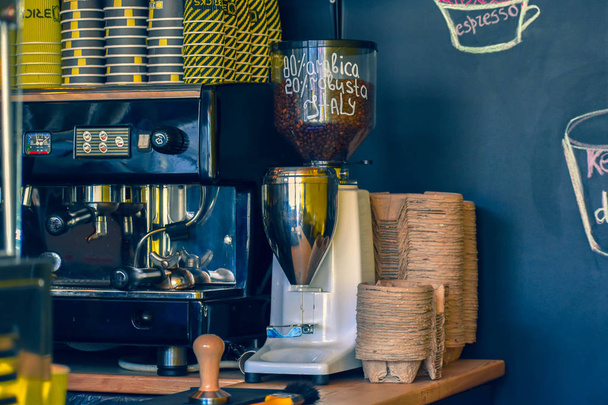 máquina de café é ao lado da mesa em um café ao lado de copos de papel para bebidas
 - Foto, Imagem