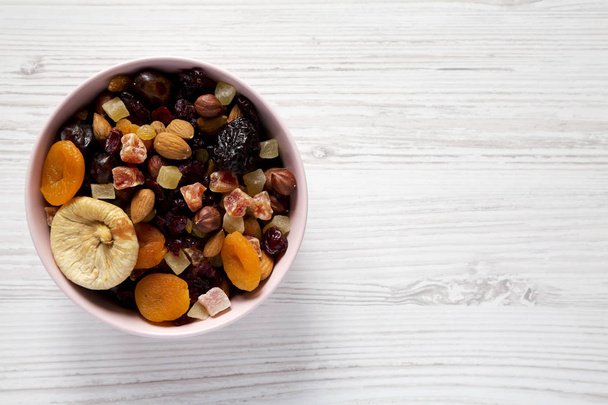 Sušené ovoce a ořechy v růžové misce nad bílým dřevěným backgronem - Fotografie, Obrázek